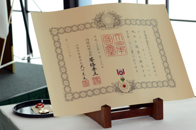 A certificate in Japanese is displayed in front of a military medal on a black tray.