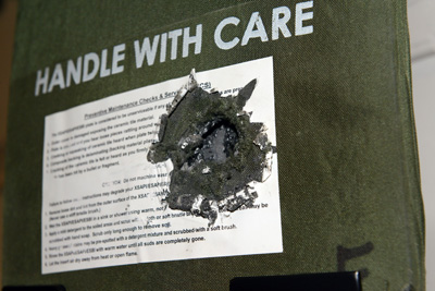 A ballistic insert shows damage from a bullet.  The words "handle with care" are printed on it.