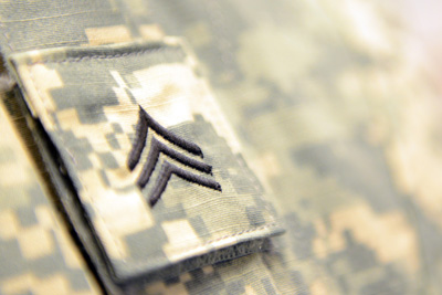 A closeup of an enlisted military rank insignia which has been embroidered onto a swatch of camouflage fabric. It is affixed to a uniform using Velcro. 