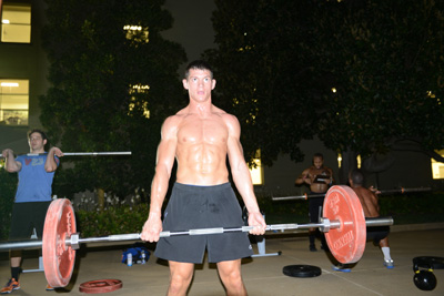A young man with no shirt on lifts a barbell.