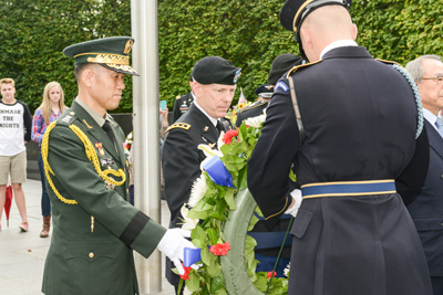 Multiple individuals in military uniforms are gathered outdoors around a wreath.