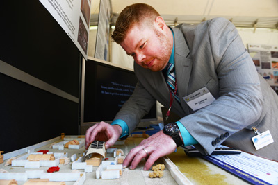 A man in a suit manipulates objects on what appears to be a 3D map, or diorama.  