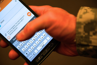 The hand of an individual in uniform holds a cell phone.  The words on the cell phone read "Your so lazy. You don't belong in the army. Who'd you pay to get in #diealreadyloser"  Some words are misspelled.