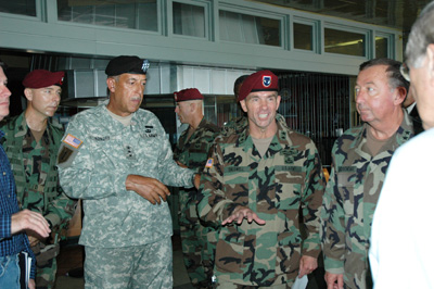 Several men in military uniforms stand together and talk.  A portion of a civilian man is seen to the right side. This is Secretary of Defense Donald Rumsfeld.