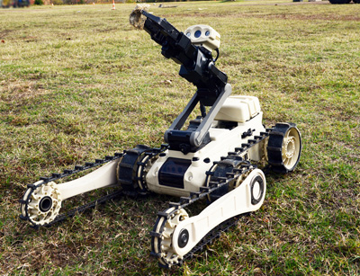 A small, tracked, autonomous robotic vehicle sits outdoors on the grass.
