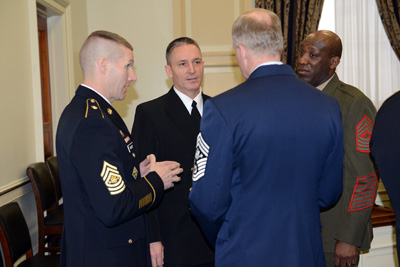 Four men in military uniforms stand in a circle and talk.