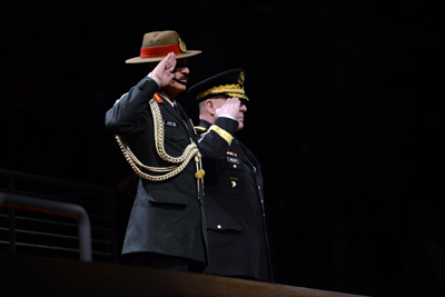 Two men in military uniforms stand next to each other in a darkened room.  They are saluting.