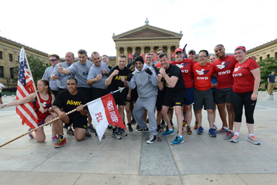 More than a dozen individuals in athletic clothing stand together with flags outdoors in front of a museum.