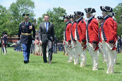 A man in a military uniform and another man in a suit walk side-by-side down a row of soldiers, who are standing at attention.