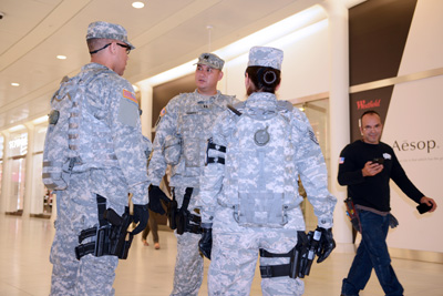 Three soldiers with weapons on their hips, stand near each other indoors and talk.