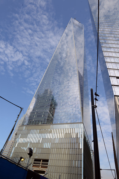 A tall glass building juts high into a cloudy blue sky.