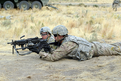 Two soldiers lie prone on the ground with their rifles pointed forward.