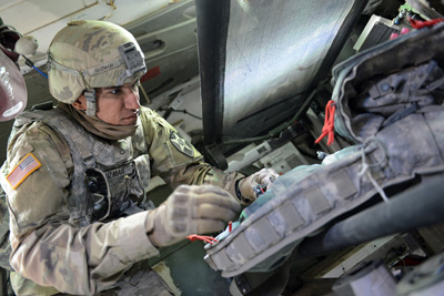 A man in a military uniform handles equipment inside a combat vehicle.