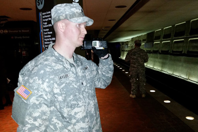 A man in a military uniform talks on a radio inside a subway station.