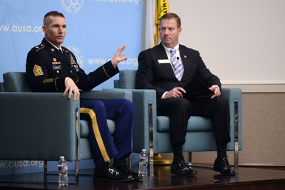 Two men, one in a military uniform and one in a suit, are seated on a stage near each other in large chairs.  A display behind them says "www.ausa.org."