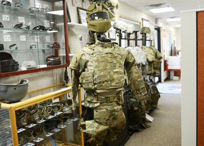 A set of combat armor hangs on a stand. Behind it is a display case that contains other articles of military clothing and gear.