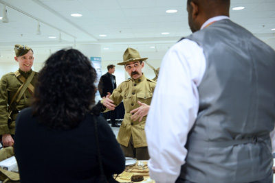 A man in an historical military uniform stands behind a table and speaks with civilians.