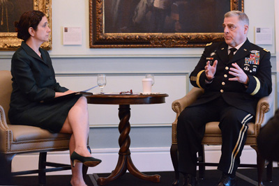 A woman in a black dress is seated across a tiny wooden table from a man in a military uniform.