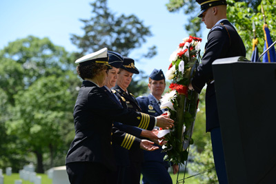 Four women in military uniform move a wreath.  A man in a military uniform stands on the other side of the wreath.