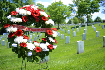 A floral wreath sits on a stand near dozens of white grave markers.
