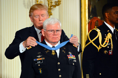 A man places a medal around the neck of a man in a military uniform.