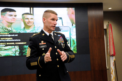 A man in military uniform stands in front a video screen.
