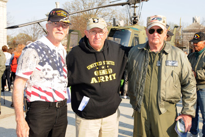 Three men stand alongside each other. Behind them is a military helicopter.