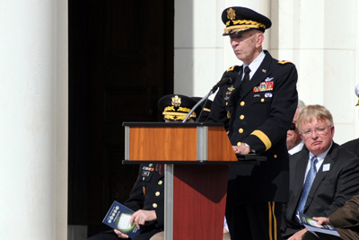 A man in military uniform stands behind a lectern.  
