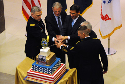 Five men, three in military uniforms and two in civilian clothing, use a sword to cut a cake.