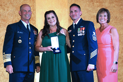 Two men in military uniforms stand alongside two women in civilian clothing. One of the women holds a box with a military medal inside.