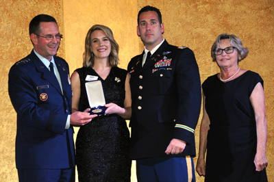 Two men in military uniforms stand alongside two women in civilian clothing. One of the women holds a box with a military medal inside.