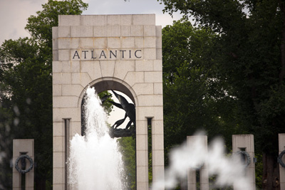 A large stone arch bears the word "Atlantic." Metal wreaths hang from other stone monuments. A fountain sprays water.