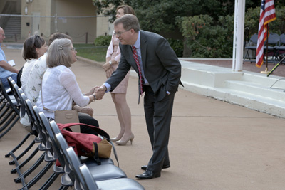A woman, who is seated outdoors, shakes hands with a man, who is in a business suit.