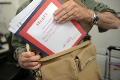 A man puts a folder into a satchel. The folder has a cover sheet, printed in red, with the word "Secret" on it.