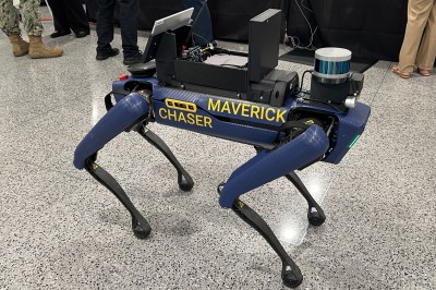 A robotic dog bears the words "MAVERICK CHASER" on the side. Mounted to its top is an array of electronic equipment.